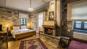 Une chambre avec un mur en pierre, une cheminée, un lit, un bureau en bois et un tapis.