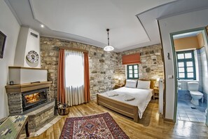 A bedroom with a stone wall, a fireplace, a bed, and a bathroom with a toilet and sink. - Gaia Guesthouse (Zagori)