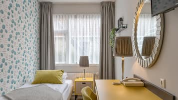 A hotel room with a bed, a desk with a telephone, a mirror, and a window with curtains.