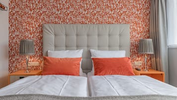 Ein Doppelbett mit weißer und orangefarbener Bettwäsche, einem gepolsterten Kopfteil und zwei Nachttischen mit Lampen.