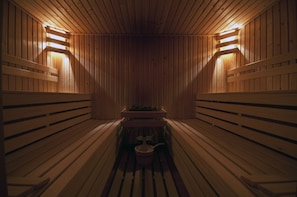 A sauna with wooden benches and benches, a central table, and two wall-mounted lights. - Hotel op Diek (Den Hoorn)
