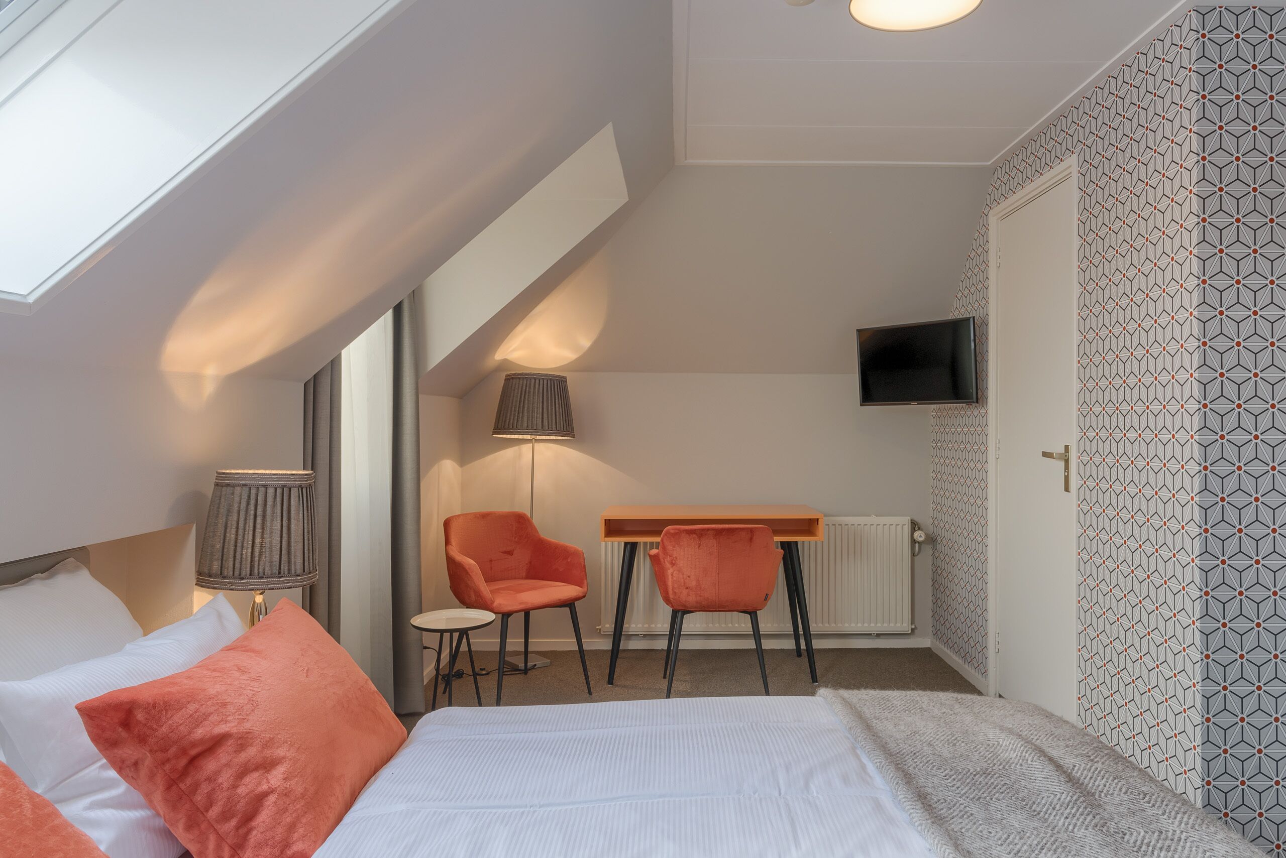 Un dormitorio con cama, dos sillas, escritorio, televisor y ventana.