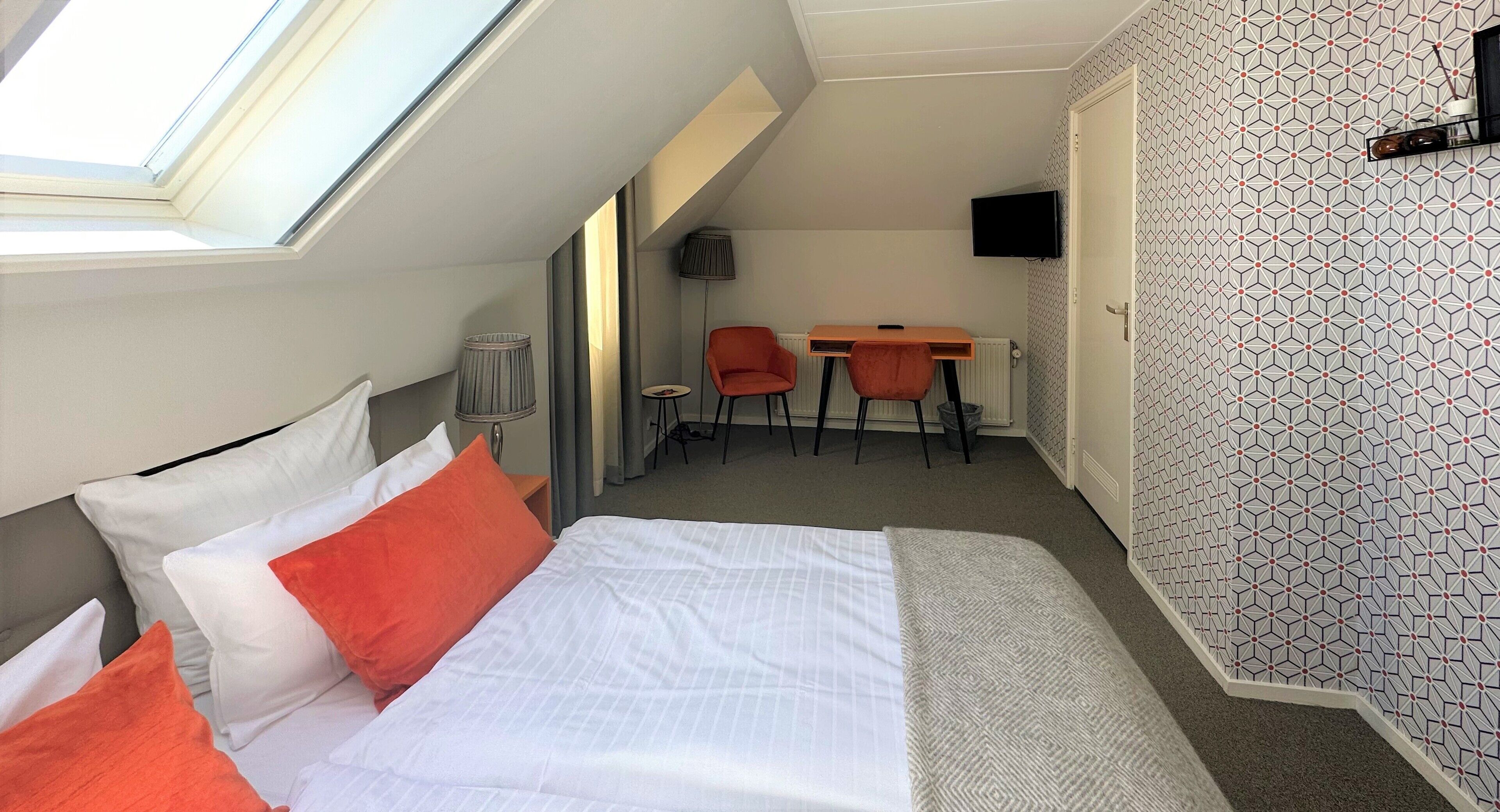 A compact hotel room with a bed, a desk, and a TV.