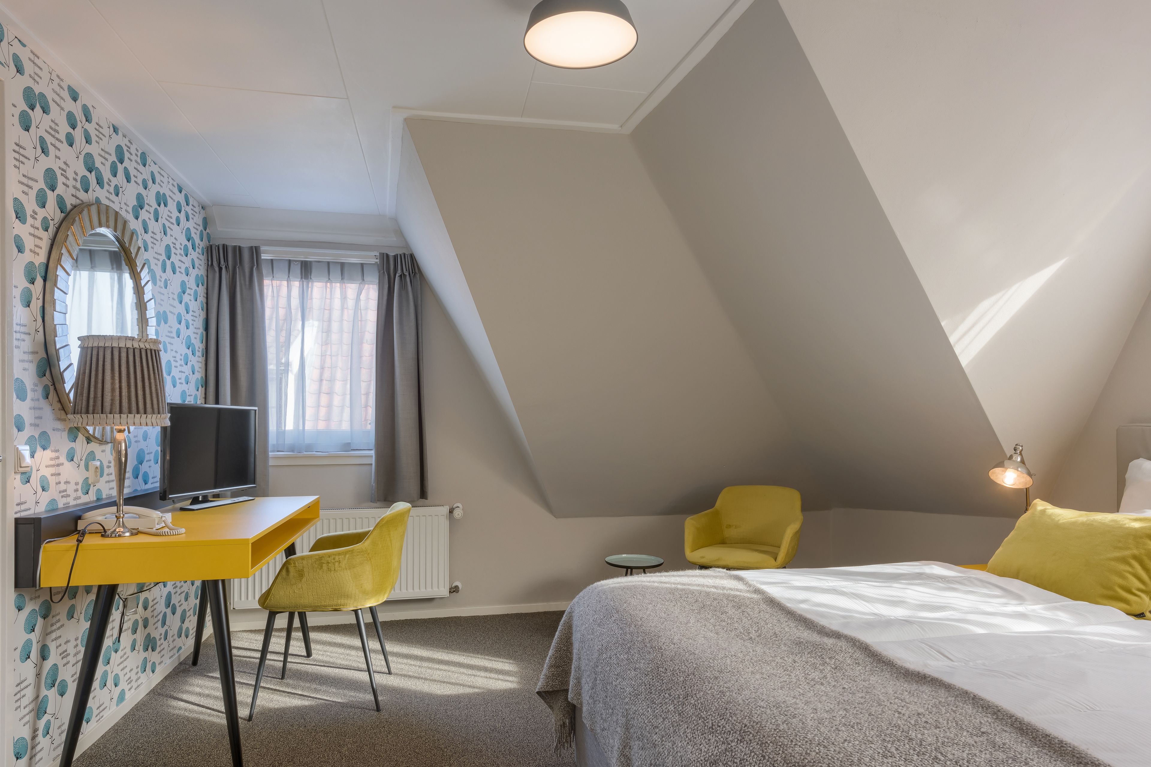 A bedroom with a bed, a desk, a chair, a mirror, and a window with curtains.