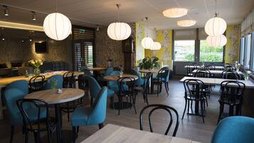 L’intérieur d’un restaurant avec des tables rondes, des chaises de couleur turquoise et des lampes suspendues.