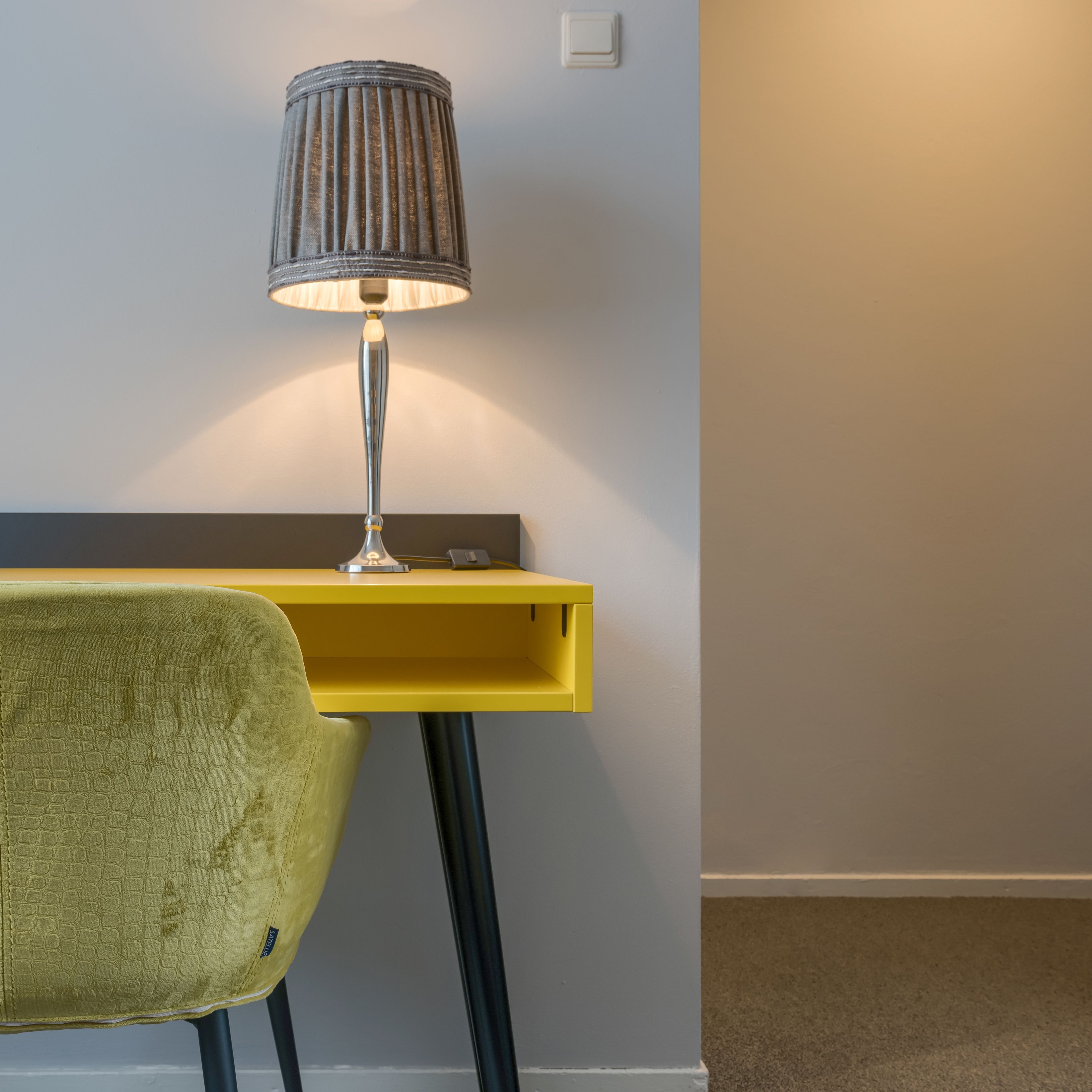 A yellow desk with a lamp and a green chair.