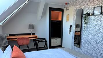 Une chambre d’hôtel avec un lit, un bureau, une chaise et un petit placard.
