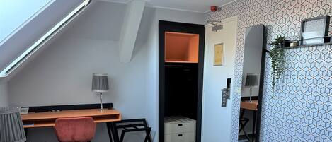A hotel room with a bed, a desk, a chair, and a small closet.