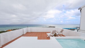 Eine Dachterrasse mit Pool, zwei weißen Liegestühlen und Meerblick.