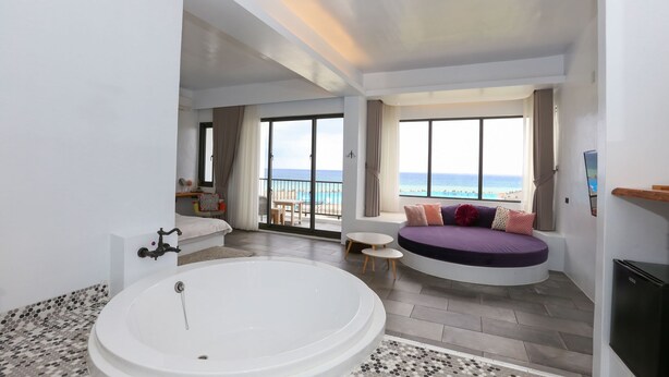 Ein modernes Badezimmer mit einer großen Badewanne, einer Sitzecke mit Blick auf den Strand und einem Balkon mit Tisch und Stühlen.