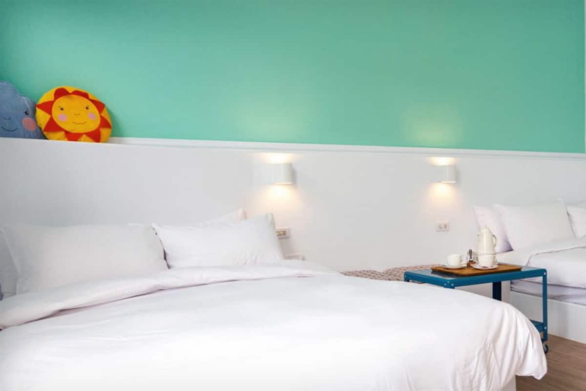 Habitación de hotel con dos camas, una mesita y una lámpara fijada a la pared.