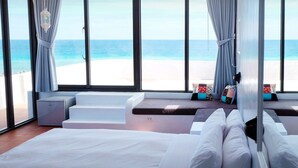 Ein Schlafzimmer mit einem großen Bett, Blick auf den Strand und einem fensterbepflanzten Fenster.