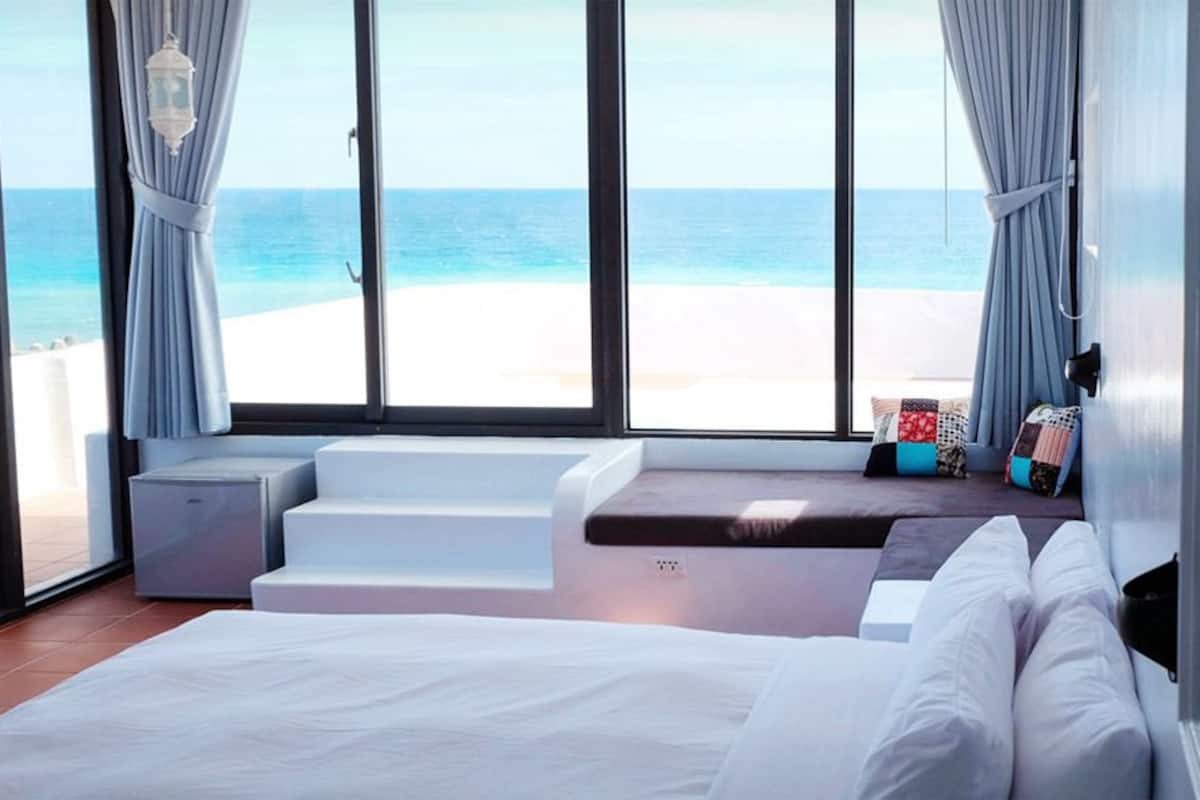 Un dormitorio con una cama grande, vistas a la playa y una ventana con cortinas.