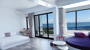 Ein modernes Hotelzimmer mit großem Balkon, einem Bett, einer Couch, einem kleinen Tisch und Meerblick.