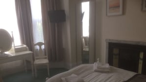 Quarto de hotel com cama, escrivaninha com cadeira, televisão de tela plana na parede e lareira.