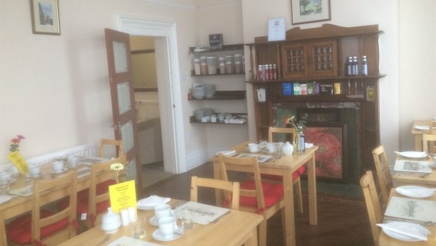 Uma sala de jantar com mesas e cadeiras de madeira, uma lareira e prateleiras com potes e garrafas.