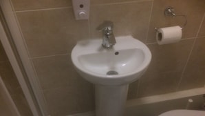 Um banheiro com pia branca de pedestal, vaso sanitário e um rolo de papel higiênico na parede.