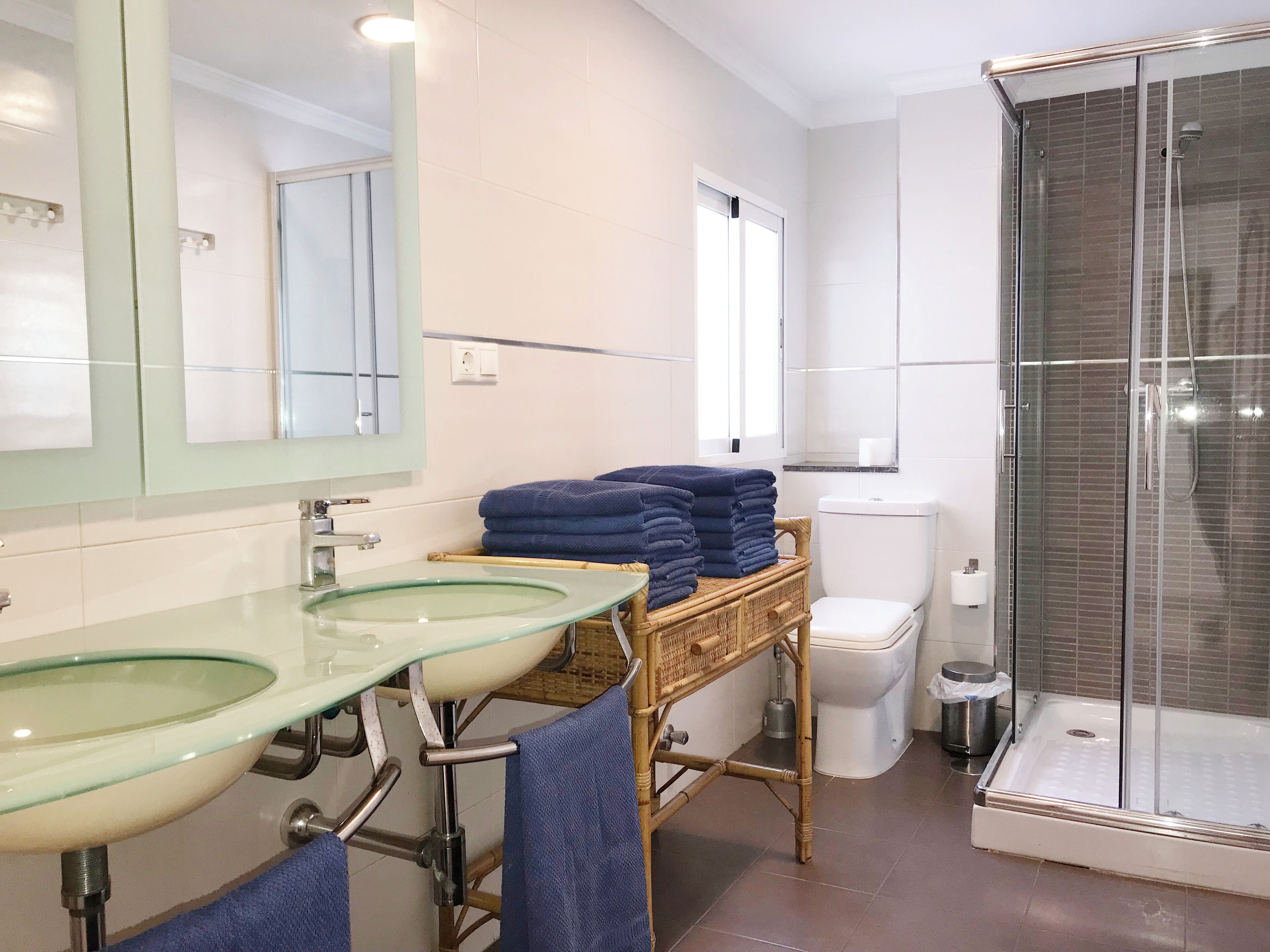 Un baño con dos lavamanos de vidrio, un inodoro y una ducha con cerramiento de vidrio.
