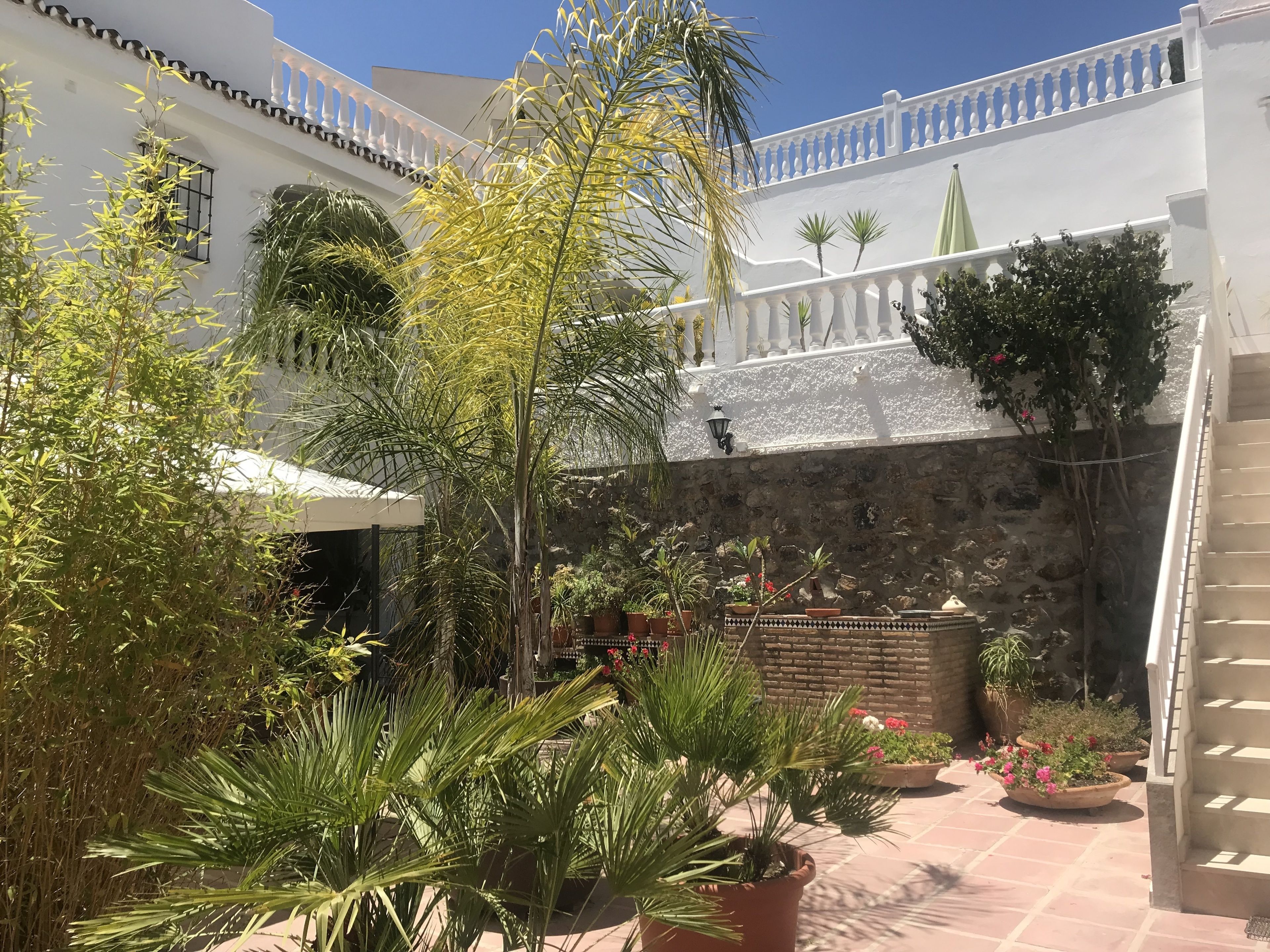 Un patio con plantas en macetas, un muro de piedra y un edificio blanco con balcones.
