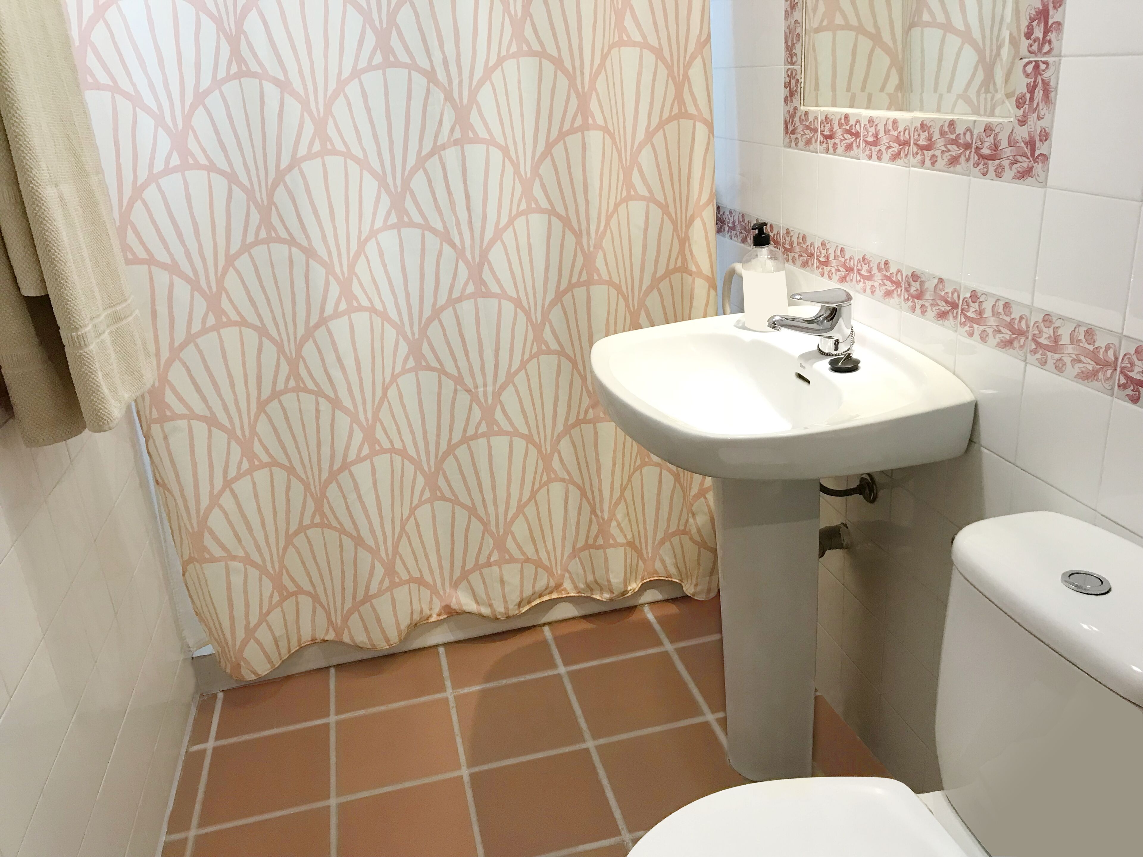 A bathroom with a white sink, a toilet, and a shower curtain with a leaf pattern.