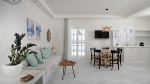 A modern living room with a sofa, coffee table, and dining area with chairs. There is a TV mounted on the wall and a window with curtains.