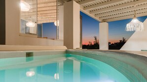A swimming pool with a view of the sunset, a hanging light fixture, and a large mirror reflecting the pool.