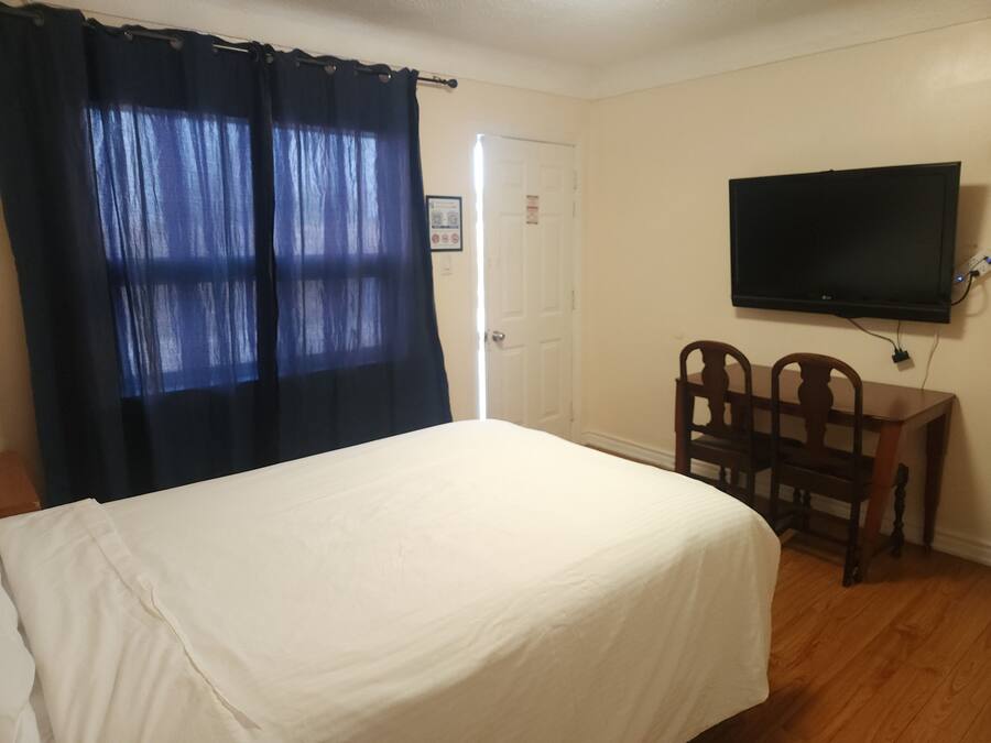 A bedroom with a bed, a desk, a chair, a television, and a door.