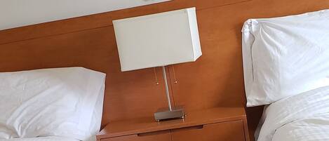 Hotellihuone, jossa on kaksi sänkyä, puinen pääty, yöpöytä lampun kanssa ja seinällä kehystetty kukka-aiheinen taideteos.