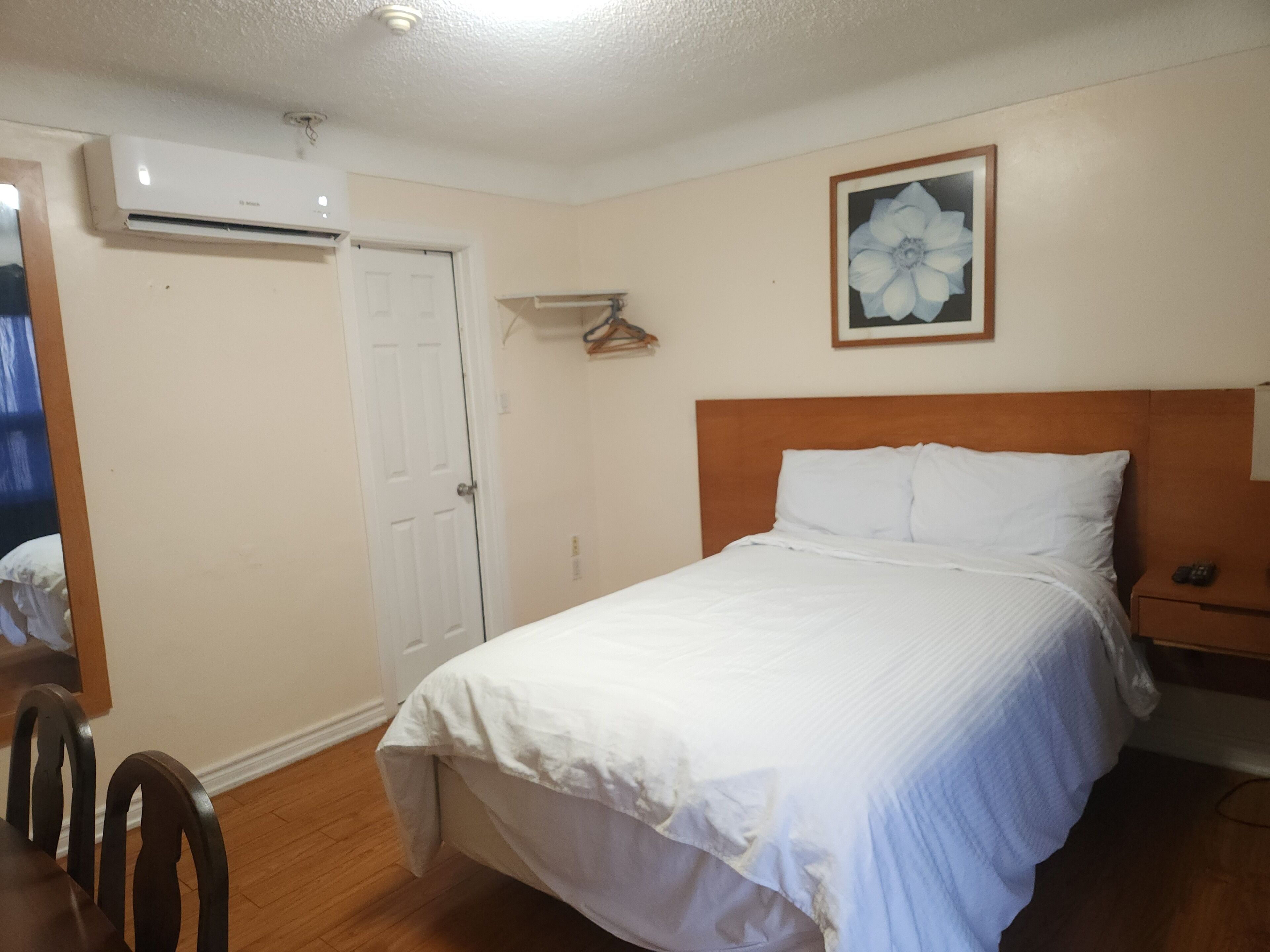 A bedroom with a bed, a wooden headboard, a white door, and a wall-mounted air conditioner.