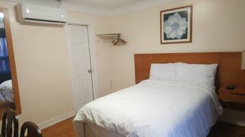 A bedroom with a bed, a wooden headboard, a white door, and a wall-mounted air conditioner.