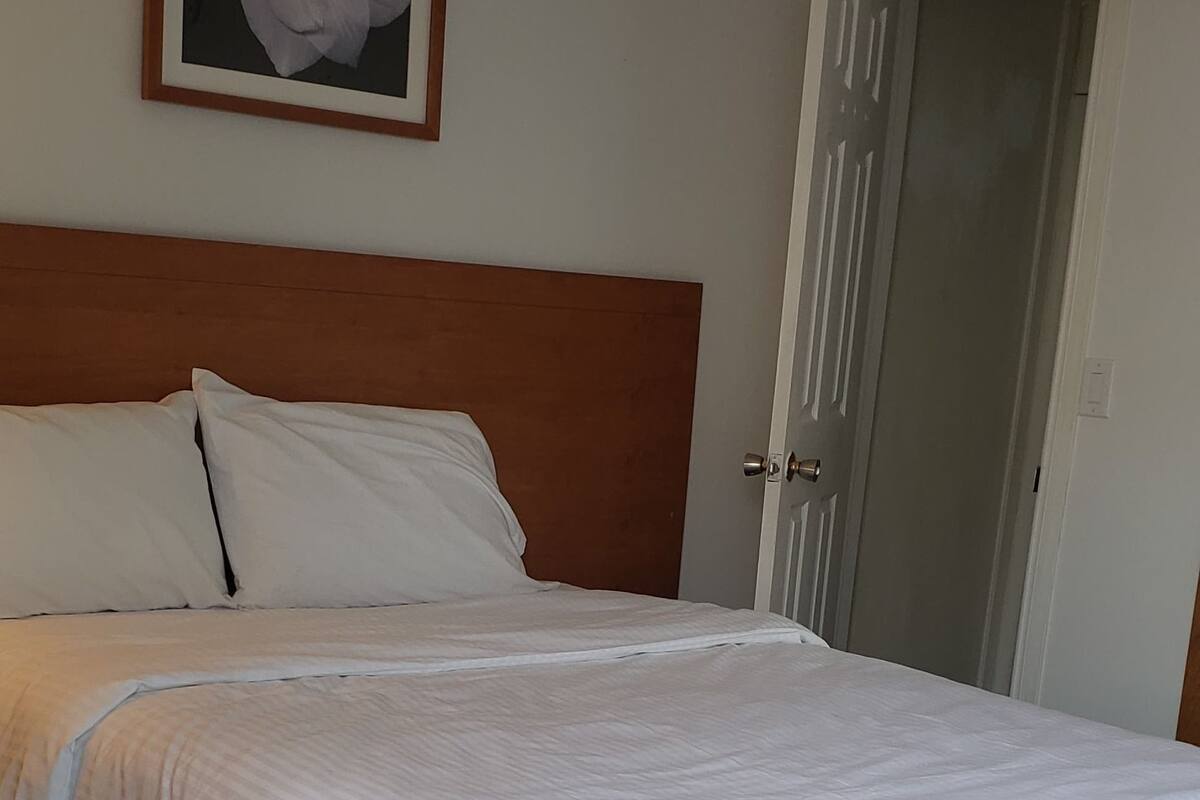 A neatly made bed with white linens, a wooden headboard, and a framed floral artwork on the wall.