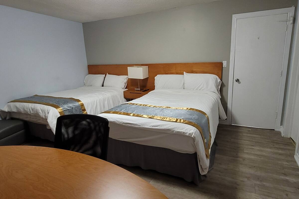 A hotel room with two beds, a wooden table, a chair, and a nightstand with a lamp.