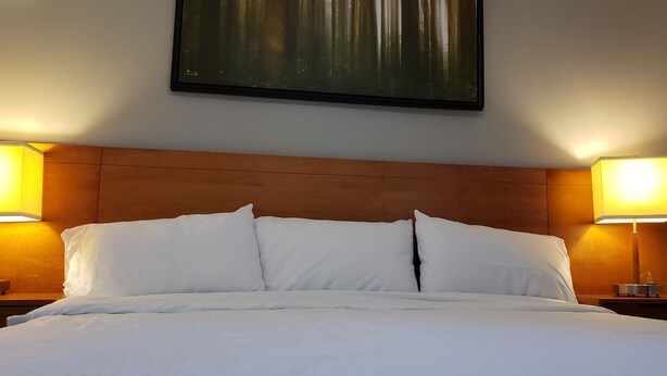 A neatly made bed with white linens and pillows, flanked by two bedside lamps on wooden nightstands. - Niagara Inn (Niagara Falls)