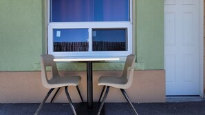 A small outdoor table with two chairs, a window with blinds, and a door. - Niagara Inn (Niagara Falls)