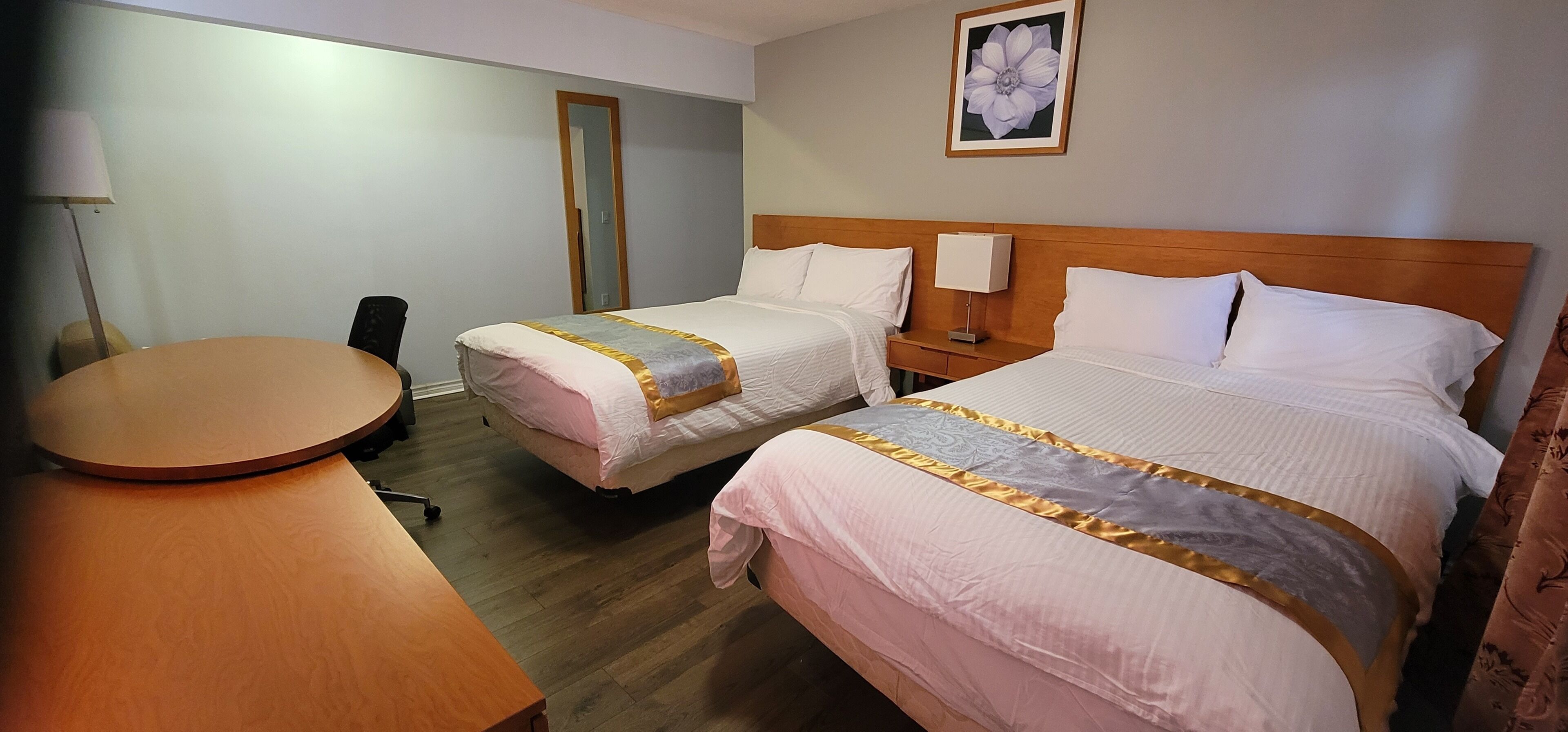 A hotel room with two beds, a wooden headboard, a round wooden table, and a lamp.