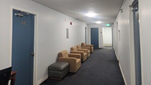 A hotel hallway with a carpeted floor, a row of beige armchairs, and doors numbered 34 and 32. - Niagara Inn (Niagara Falls)