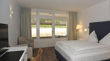 Ein Hotelzimmer mit Bett, Schreibtisch, Stuhl, Fernseher und Blick auf einen Garten durch die Tür.