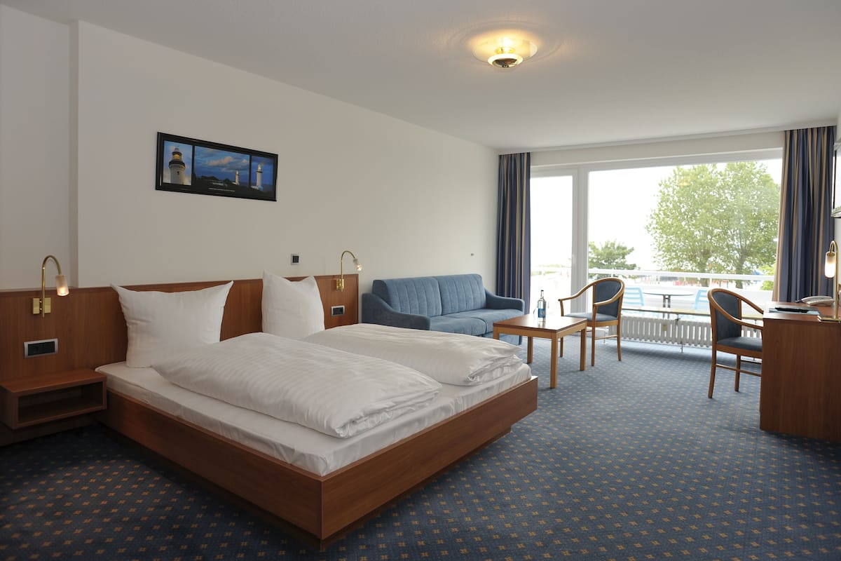A hotel room with a large bed, a sofa, a desk, and a view of the outdoors.