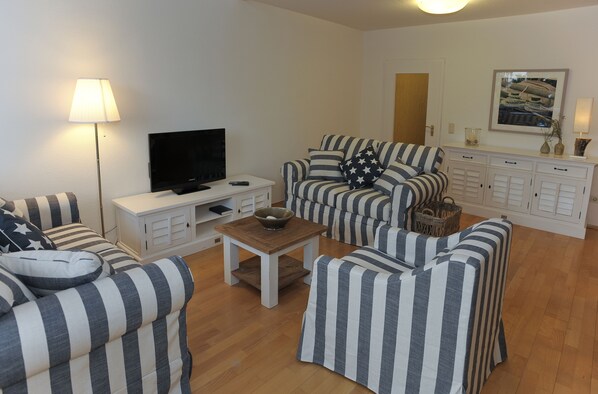 A living room with striped sofas, a TV, a small table, and a cabinet.