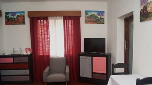 A room with a sofa, a TV on a cabinet, a table with a white tablecloth, and two paintings on the wall. - Villa Mahefa (Antananarivo)