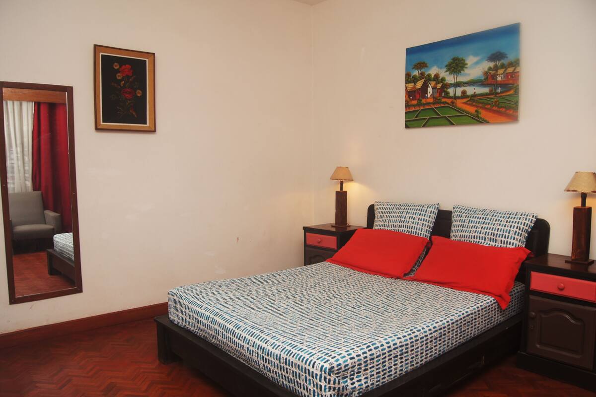 A bedroom with a bed, two bedside tables, a nightstand, a mirror, and a painting on the wall.