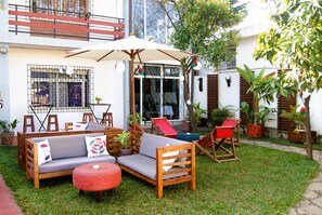 A patio area with a wooden sofa, red chairs, and a table. There are potted plants and a large umbrella providing shade. - Villa Mahefa (Antananarivo)