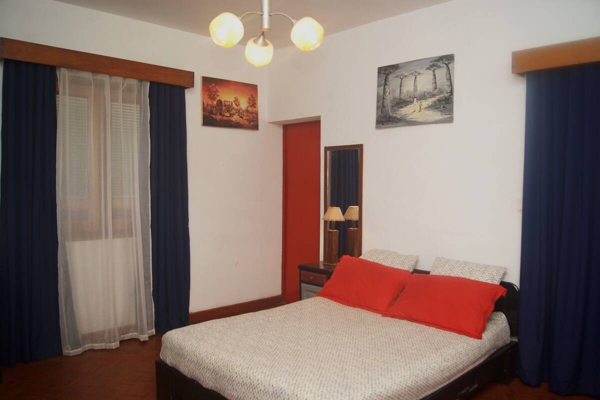 A bedroom with a bed, a nightstand, a mirror, and two paintings on the wall.