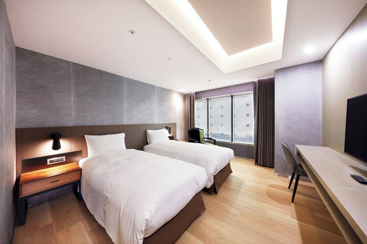 Una habitación de hotel moderna con dos camas, un escritorio y un ventanal grande.