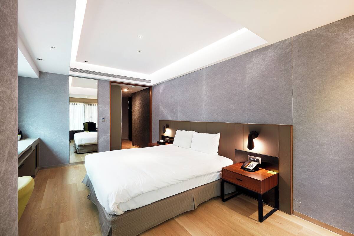 Una habitación de hotel moderna con una cama grande, mesitas de noche, un escritorio y un espejo.