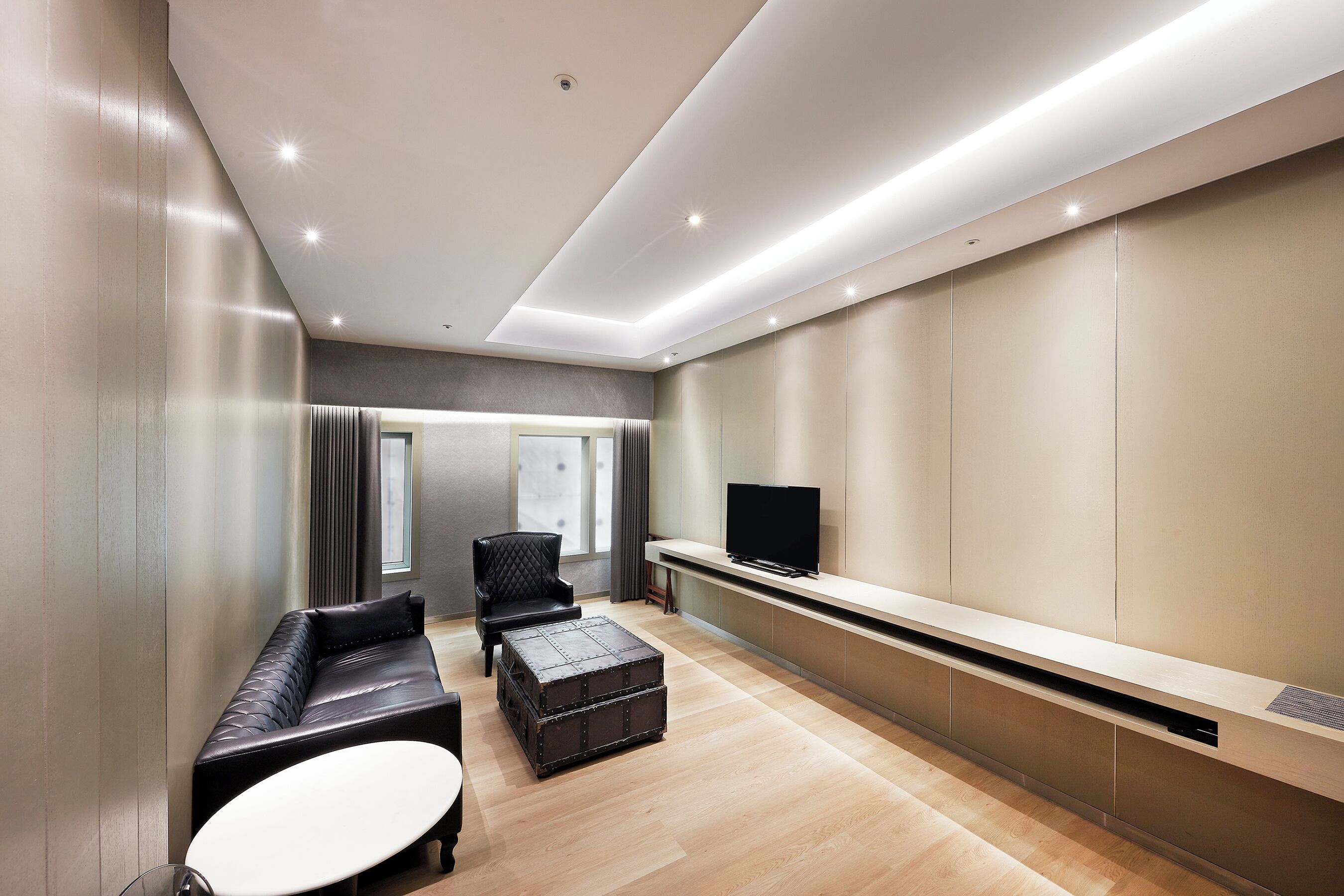 A modern living room with a sofa, ottoman, and a flat-screen TV on a built-in shelf.