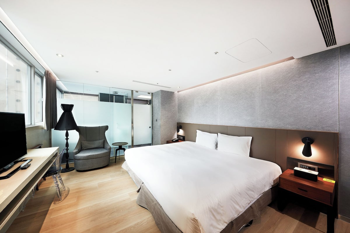 Una habitación de hotel moderna con una cama grande, una mesita de noche, una lámpara y un televisor sobre un escritorio.