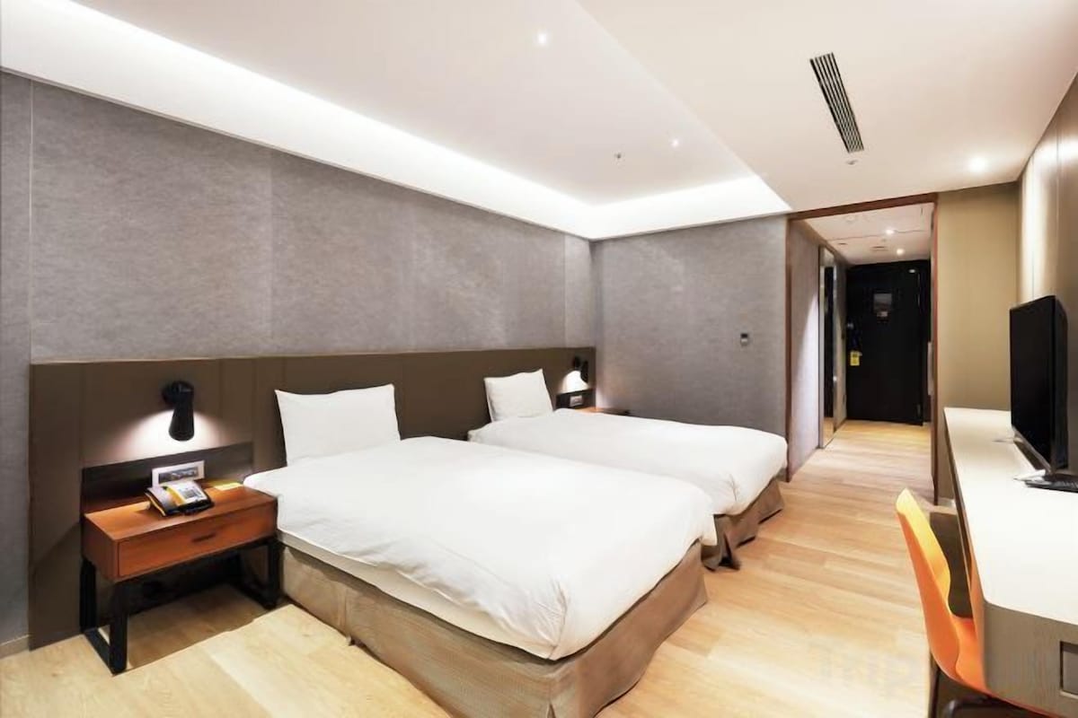 Une chambre d’hôtel avec deux lits, un bureau, une chaise, une table de chevet et un téléviseur.