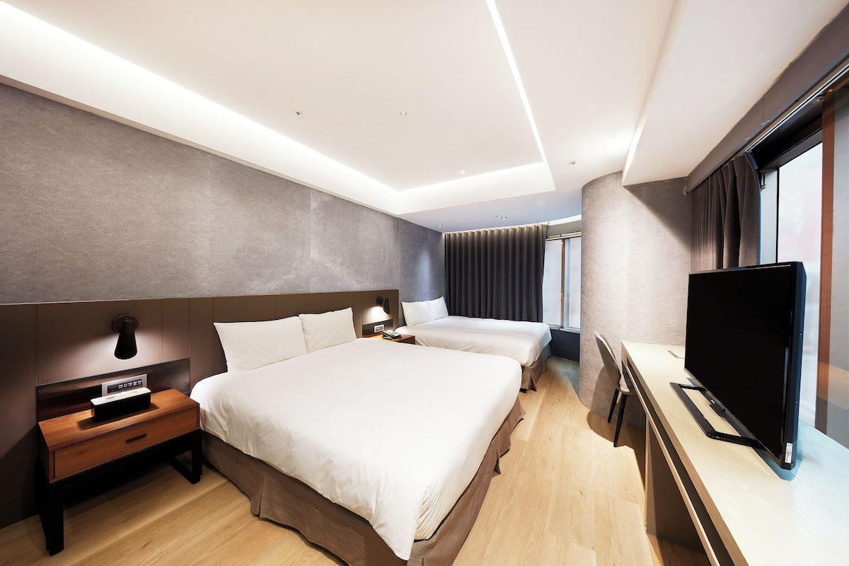 Una habitación de hotel moderna con una cama grande, mesitas de noche, un televisor de pantalla plana y un ventanal amplio.