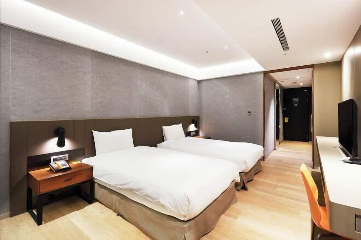 Una habitación de hotel moderna con dos camas, un escritorio, una silla y un televisor.